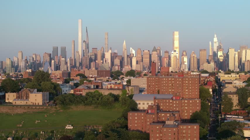 Aerial view of suburban neighborhood with apartment buildings and trees, overlooking Manhattan skyline at sunset.