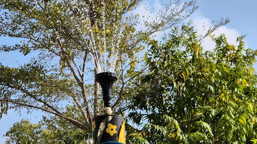 Outdoor Garden Water Fountain Spraying Water Against Blue Sky and Green Trees