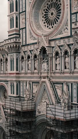 Aerial video of Santa Maria del Fiore Cathedral facade rising to reveal the Florence cityscape under an overcast sky.