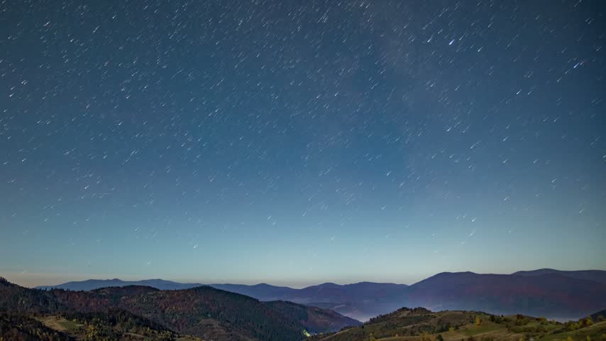 Nigh starry sky above forestry mountains and hills at dusk