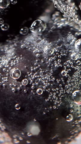 Extreme macro close up of a fresh dark fruit or berry immersed in carbonated sparkling water with sparkling gas bubbles clinging to the skin.