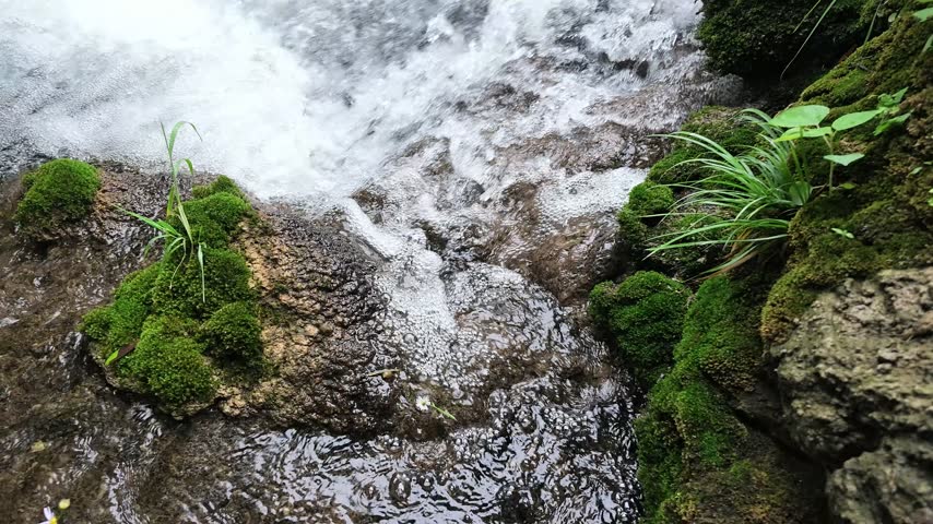 A small creek waterfall with slow-motion flowing water over rocks, surrounded by green forest in Hubei, China. Peaceful nature scene.