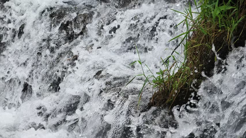 A small creek waterfall with slow-motion flowing water over rocks, surrounded by green forest in Hubei, China. Peaceful nature scene.