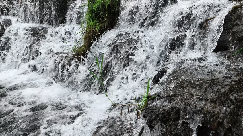 A small creek waterfall with slow-motion flowing water over rocks, surrounded by green forest in Hubei, China. Peaceful nature scene.