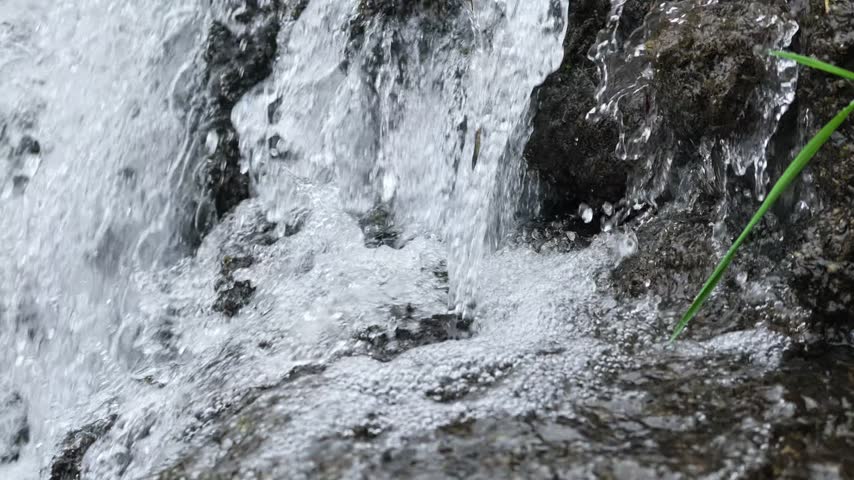 A small creek waterfall with slow-motion flowing water over rocks, surrounded by green forest in Hubei, China. Peaceful nature scene.