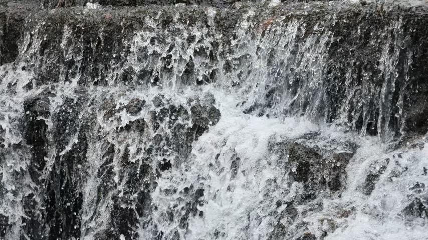 A small creek waterfall with slow-motion flowing water over rocks, surrounded by green forest in Hubei, China. Peaceful nature scene.