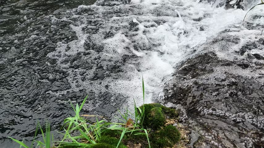 A small creek waterfall with slow-motion flowing water over rocks, surrounded by green forest in Hubei, China. Peaceful nature scene.