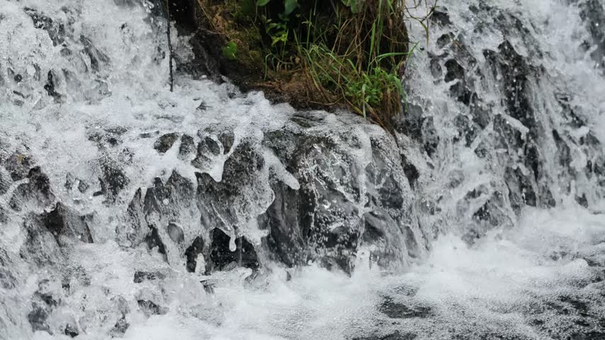 A small creek waterfall with slow-motion flowing water over rocks, surrounded by green forest in Hubei, China. Peaceful nature scene.