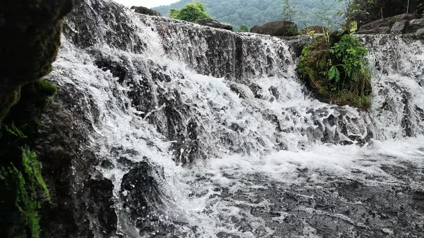 A small creek waterfall with slow-motion flowing water over rocks, surrounded by green forest in Hubei, China. Peaceful nature scene.