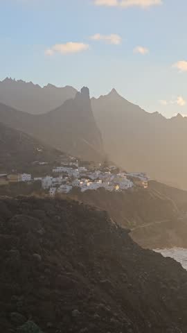 The last warm light of the day settles over the Anaga coastline near Benijo with a cliffside village catching the glow. A closing phone view from the viewpoint road.