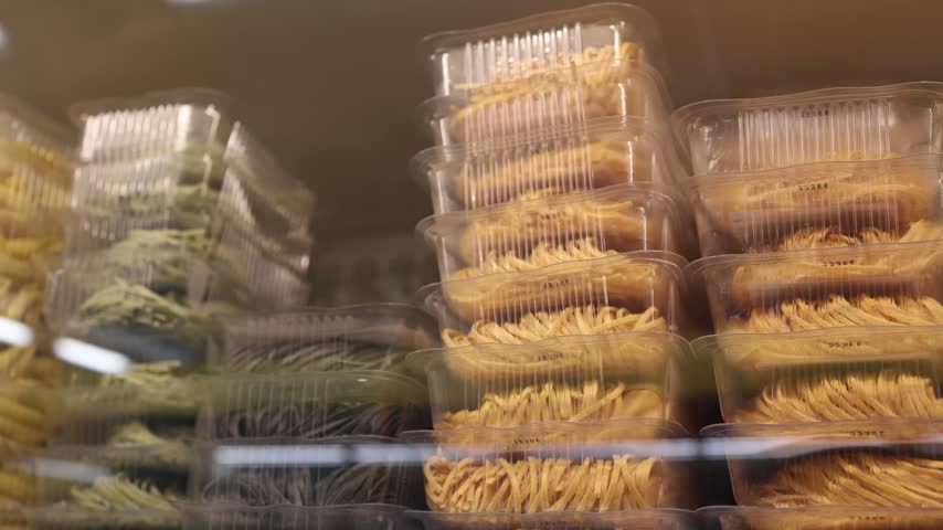 Fresh handmade pasta in clear containers displayed behind glass showing colorful noodles traditional Italian food variety grocery retail and ready to cook meal selections