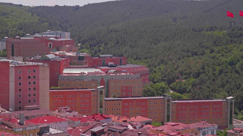 High-angle shot showcasing the extensive campus of Yeditepe University nestled directly at the base of Kayisdagi Mountain in Istanbul. Detailed view highlighting academic buildings, green surroundings, university infrastructure, and urban backdrop under clear daylight.