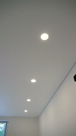 Upward view of a smooth white stretch ceiling with a row of warm recessed LED downlights in a modern renovated room.
