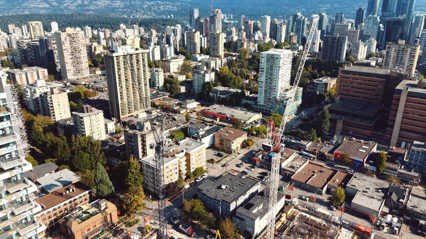 Aerial drone footage capturing construction cranes rising beside a hotel tower in Vancouver