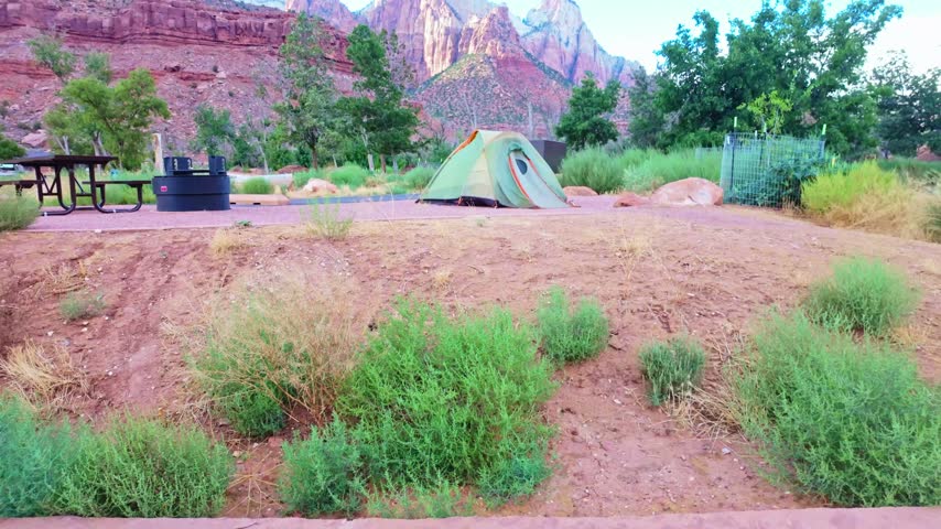 A camping tent sits at a campground with sweeping panoramic views of Zion National Park formations behind