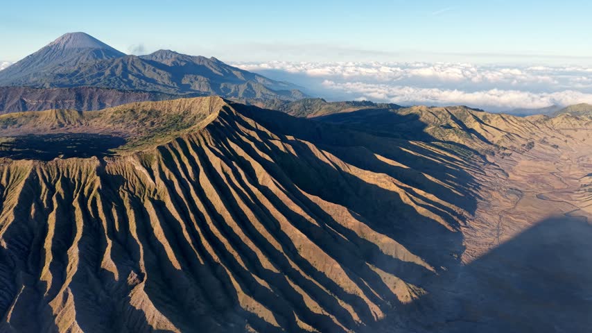 Sunlit volcanic ridges at Mount Bromo with low clouds and long morning shadows