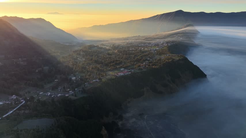 Golden sun kisses misty mountainside valley. Low clouds swirl around forested hills
