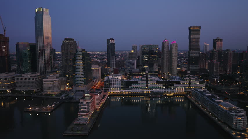 Beautiful blue hour light settling across Jersey City, Superb Quality, Aerial view shot of Jersey City, New Jersey, USA showing the urban skyline and waterfront in cool evening tones with glowing buildings, crisp architectural detail and a calm city atmosphere, crystal clear crisp image