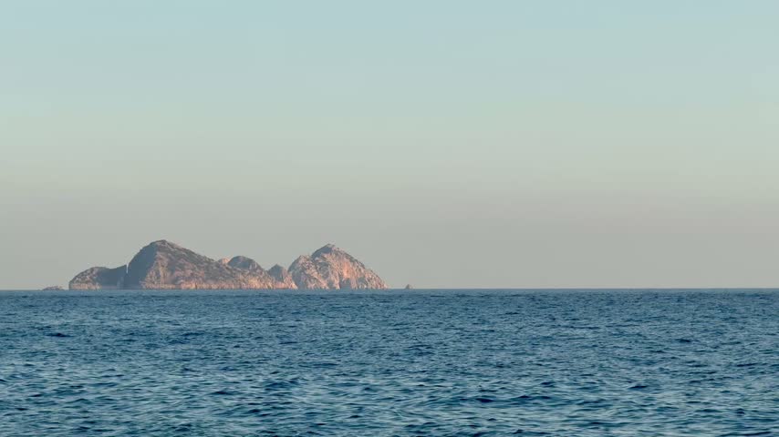 Suluada Island in the Mediterranean sea distant view on sunny day in Antalya Turkey. The rocky silhouette of uninhabited Suluada Island on the horizon of the blue Mediterranean Sea. Also known as the Turkish Maldives, the coastal landmark is captured on a calm sunny day in Antalya Province, Turkey, creating a peaceful minimalistic seascape background with ample copy space.