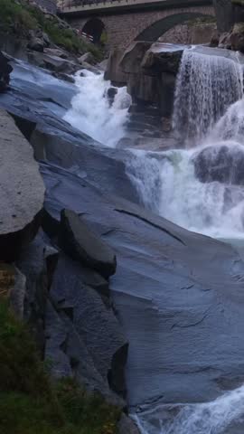 Close-up view of a cascading waterfall surrounded by rugged rocks in a Swiss mountain gorge.