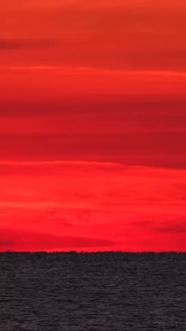 A sunset unfolds over the ocean, with shades of orange, red, and blue illuminating the sky. The horizon meets the water, creating a dramatic scene at dusk.