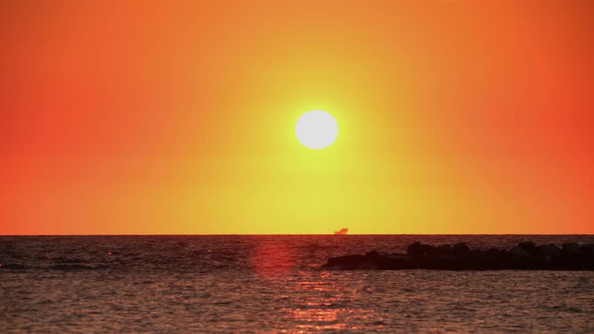 A sunset displays vibrant orange colors over the ocean. The sun sets on the horizon, casting reflections on the water and creating a colorful skyline.