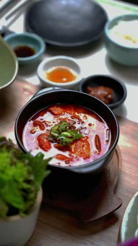 Spicy Korean tofu stew with green onion in black pot served with rice and side dishes.