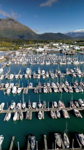 Aerial view flying over a crowded harbor full of boats and yachts with mountains in the background in Seward.