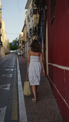 A person walks down a narrow street in a small town. The buildings are colorful, and the evening light creates a warm atmosphere. Shops are closed, and the street is empty.