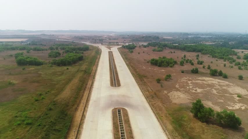 Aerial drone footage of a straight concrete highway corridor and transportation intersection passing through an open terrain landscape.