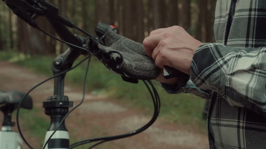 Woman putting on a cycling glove beside an electric bicycle on a forest path while preparing for a ride