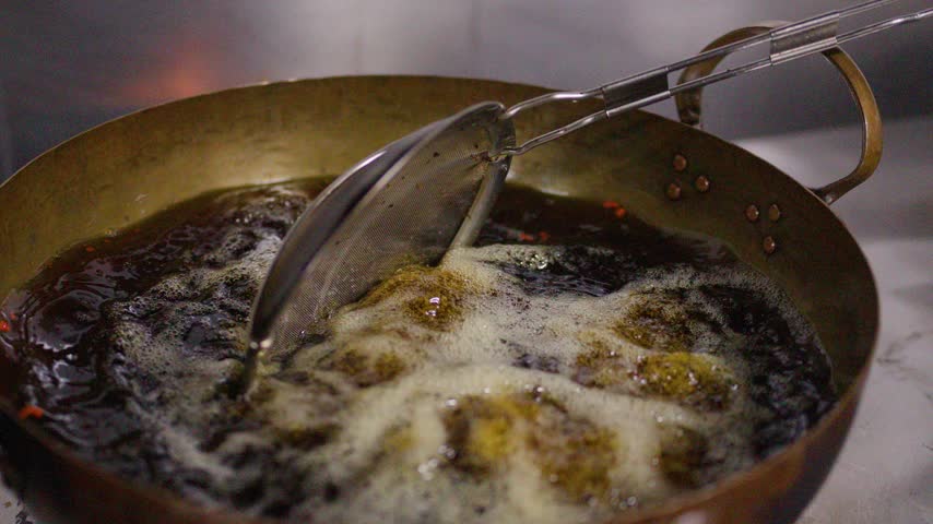 Close-up view of food frying in a large brass karahi wok with boiling hot oil.