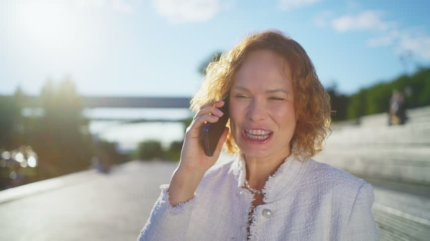 Close portrait of a woman with visible dental braces smiling during a smartphone conversation in warm outdoor light.