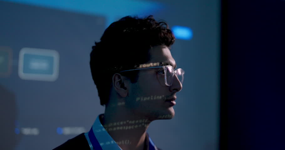 Adult male technology professional turns slightly while watching projected software dashboard, listening to system briefing and reviewing digital strategy information during business meeting.