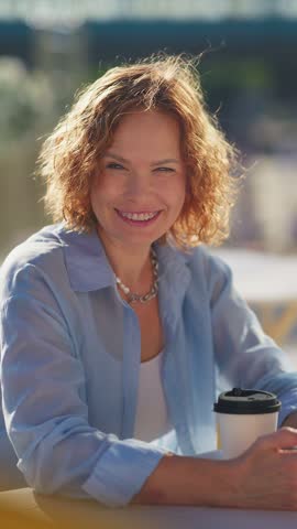 Vertical close portrait of a woman with dental braces resting her chin on her hand at a cafe, then smiling.