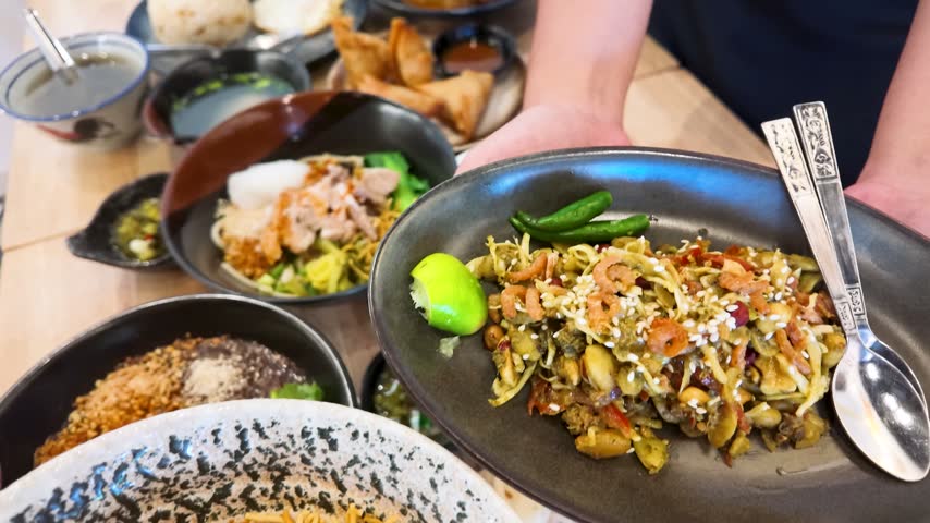 High angle close-up of hands serving crispy Shan noodles with prawns and Burmese salad.
