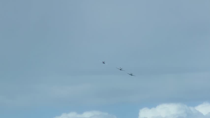 Three historic warbirds perform a formation flight against a cloudy sky during an airshow.