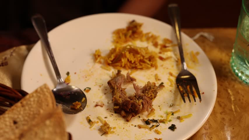 Overhead view of pouring white sauce from a spoon onto Indian biryani rice leftovers.