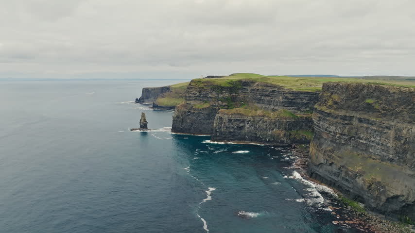 Layered sea cliffs and Atlantic coastline at the Cliffs of Moher in County Clare, Ireland, form an aerial sightseeing view with a rock stack and white surf.