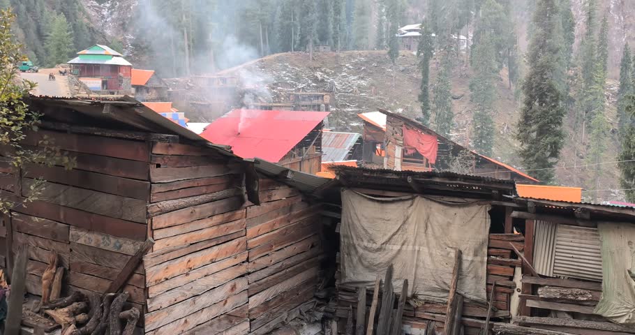 Rustic wooden mountain village houses with smoking chimneys in a cold forest landscape