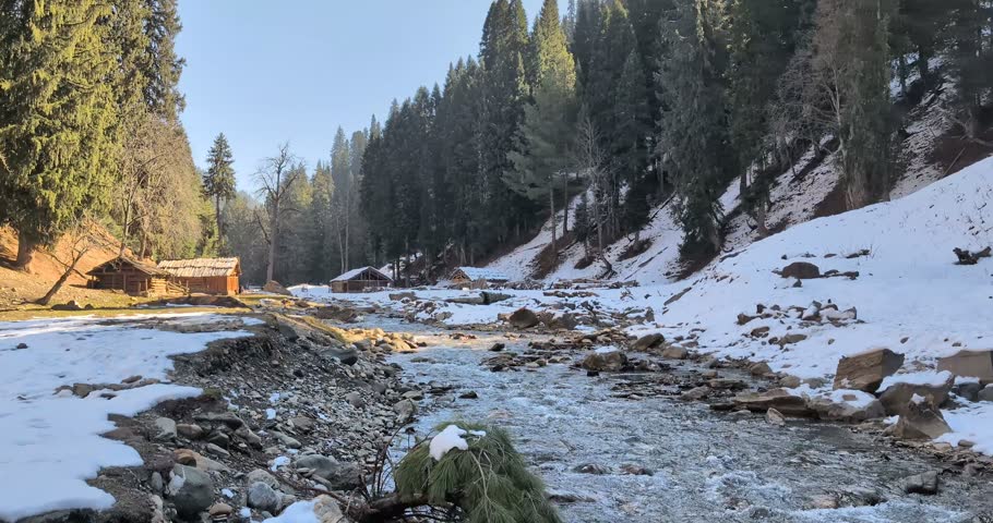Frozen river in snow-covered forest with wooden bridge and rocky terrain