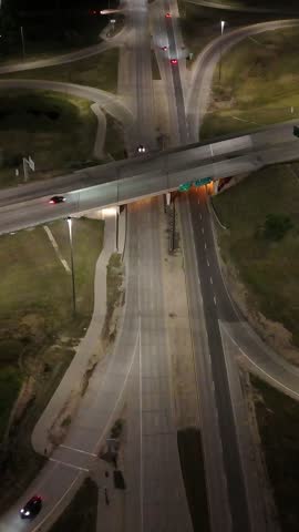 Vertical static night drone aerial looking down at the South Perimeter Highway and Pembina Highway cloverleaf overpass showing moving traffic in Winnipeg, Manitoba, Canada.