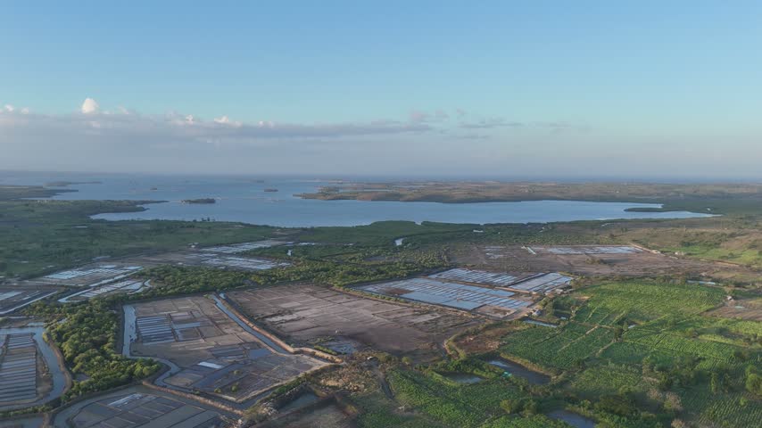 Aerial view of vast salt farms and aquaculture ponds near a calm bay under a bright blue sky
