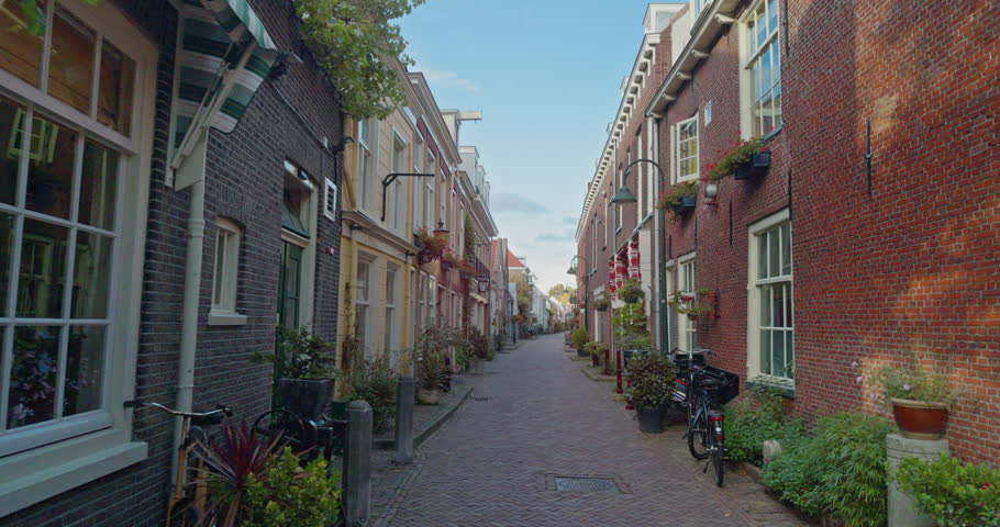 Cobblestone street road flanked by traditional Dutch townhouses in Delft, Netherlands, Europe with vibrant flower bloom boxes, bicycles parked along facades, and historic brick architecture...