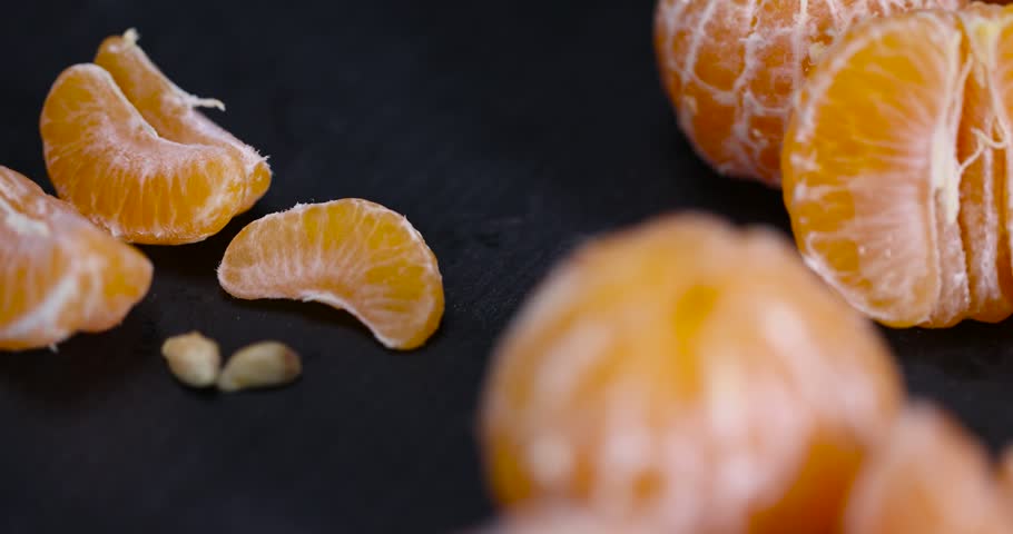 sliced juicy peeled orange tangerine on a black table, ripe orange small mandarin without peel on a black slate board, tangerine divided into small slices