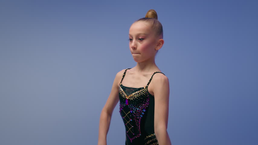 Talented Caucasian little girl gymnast acrobat juggler spinning juggling clubs in blue studio child athlete schoolgirl kid dancer practicing artistic elements rotate spin exercise indoor dance school