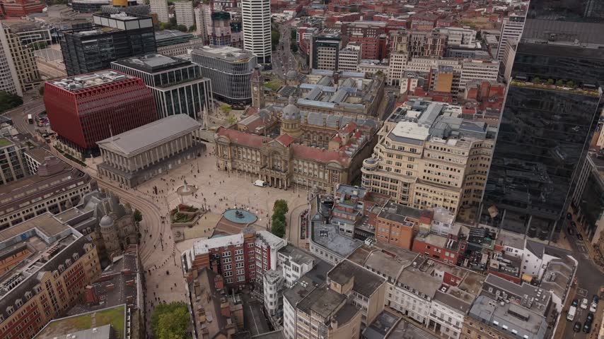 Aerial view across Birmingham city centre featuring a prominent black glass skyscraper surrounded by modern high-rise buildings, historic architecture, busy public spaces and the extensive urban lands