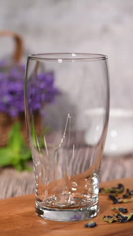 Blue butterfly pea tea is poured into a tall clear glass, gradually filling it with a deep purple herbal infusion and a light layer of foam. Part 2 of a drink preparation series. Vertical video. Real time.