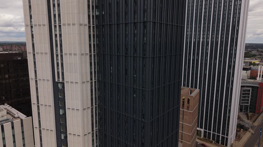 Drone ascends alongside modern high-rise buildings in Birmingham, gradually revealing more of the city skyline and surrounding urban landscape from an elevated perspective.