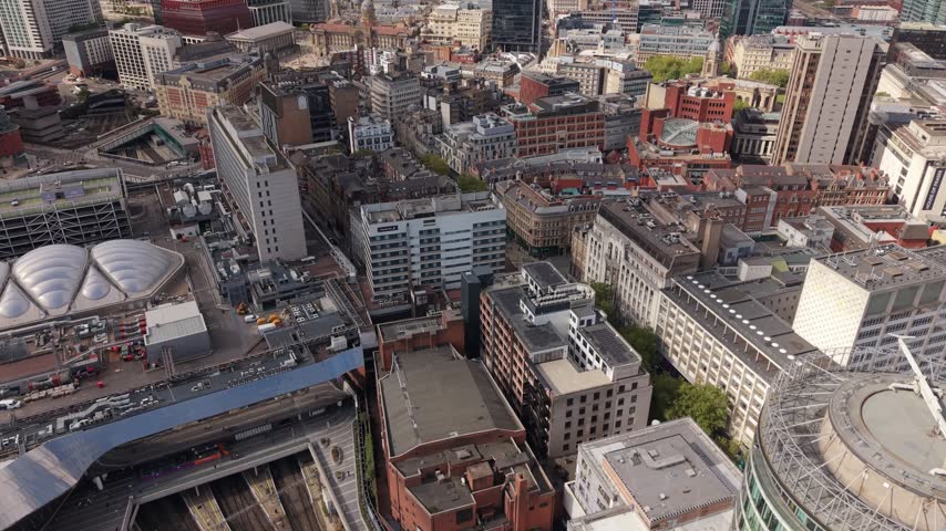 Aerial view over Birmingham city centre revealing dense urban development with historic brick buildings, modern offices, high-rise structures, streets and rooftops across the British city.